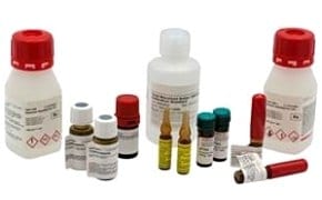 A collection of various chemical bottles and containers with different sizes, shapes, and colors. Some bottles have red caps and labels with hazard symbols indicating flammable and corrosive substances. There are also small vials with yellow liquid, alongside tubes with white caps.