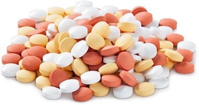 Solid Formulation Strategies: a large pile of assorted tablets and capsules in various colors, including white, yellow, and red.