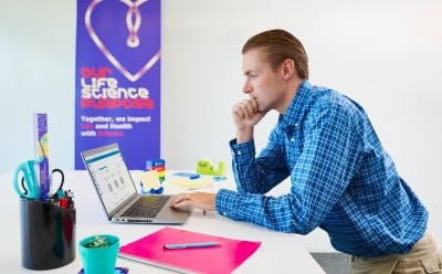 Scientist sitting at a desk, looking at a computer with data.