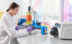 A scientist works on a bioreactor while sitting at a white counter next to a window.