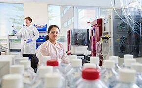 One male and one female scientist working in an analytical development lab for biologics preparing and analyzing samples with many bottles with white and red caps.