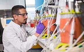 A man wearing safety glasses operating a 3-liter single-use bioreactor in a laboratory filled with multiple 3 liter single-use bioreactors.