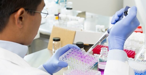 A male laboratory technician with asiatic semblance is doing an experiment with liquids and a syringe.