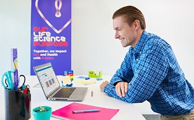 Scientist sitting at a desk in an office, looking at data on a laptop computer.