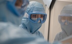 Two operators, close up in personal protective equipment at a laminar flow cabinet preparing reagents